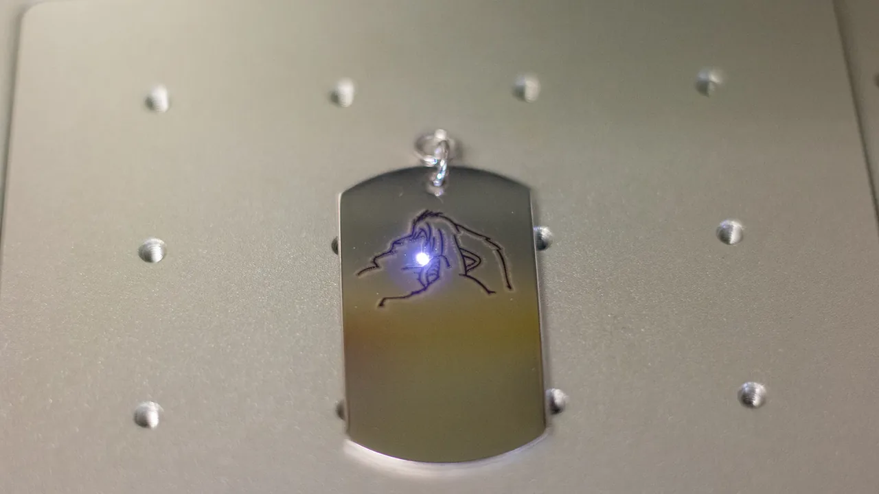 Dettaglio ravvicinato di un pendente inciso al laser, con il punto luminoso del laser